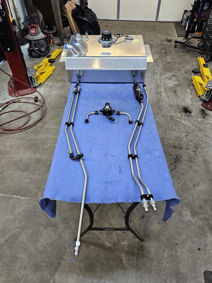 Aluminum fuel tank with in-tank pump, stainless hard lines, filter and regulator laid out on a shop bench